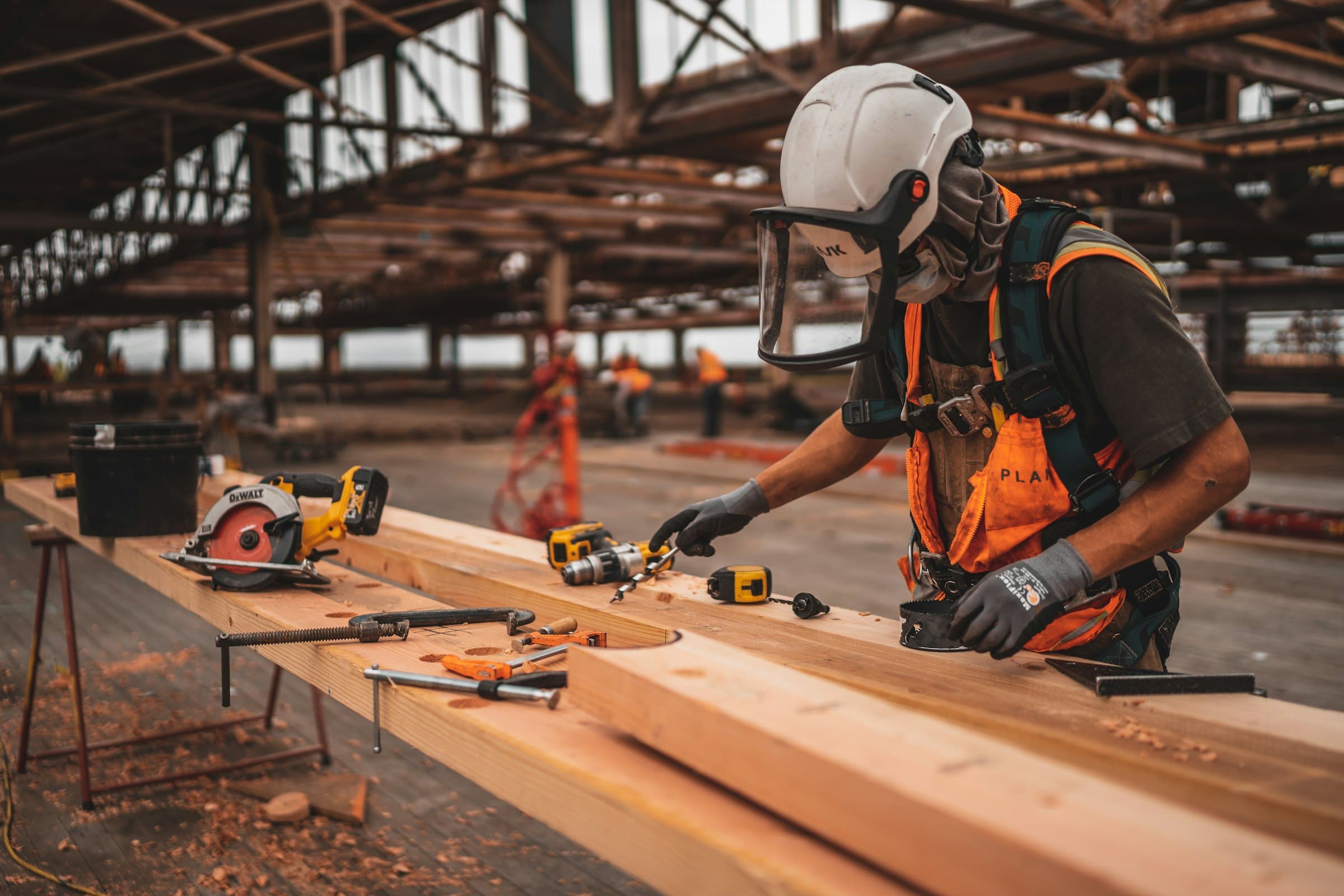 Operative in full PPE cutting timber on a workbench under a steel roof